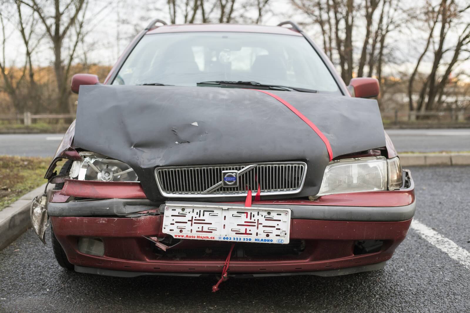Red Volvo wagon parked in a lot, its hood crumpled by a recent crash