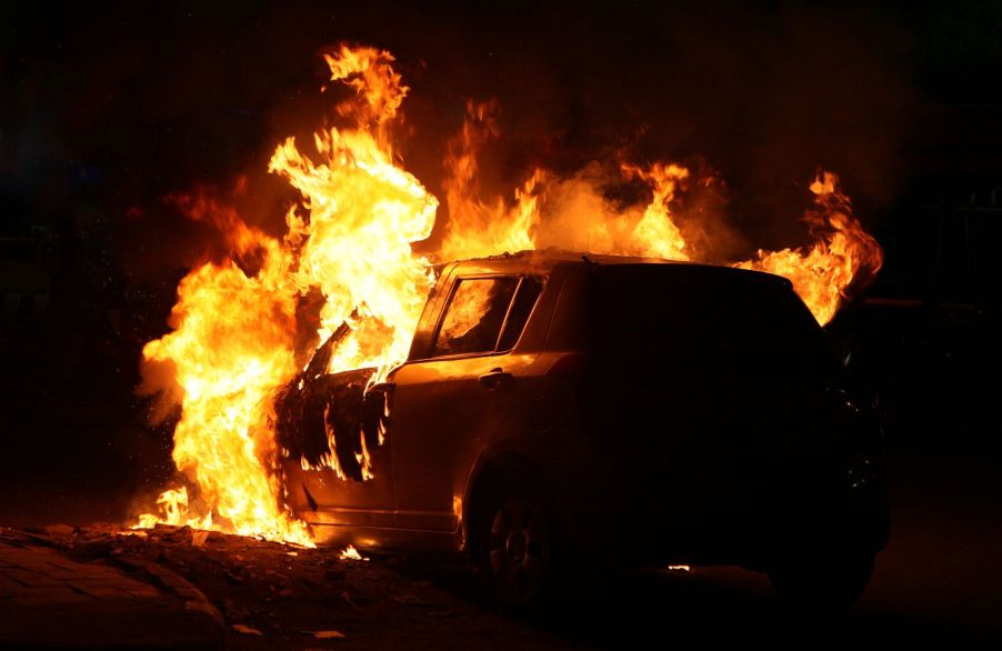 A car engulfed in flames on the side of the road at night
