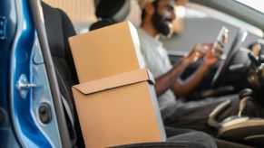 Blurred delivery driver sitting in their seat with right front door open revealing cardboard boxes on passenger seat