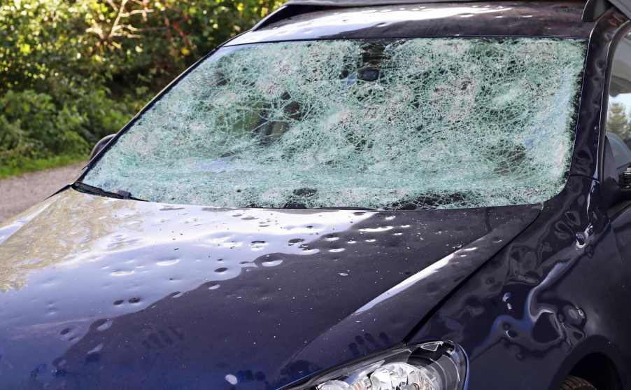 A hail damaged car with a very cracked windshield in close left front view