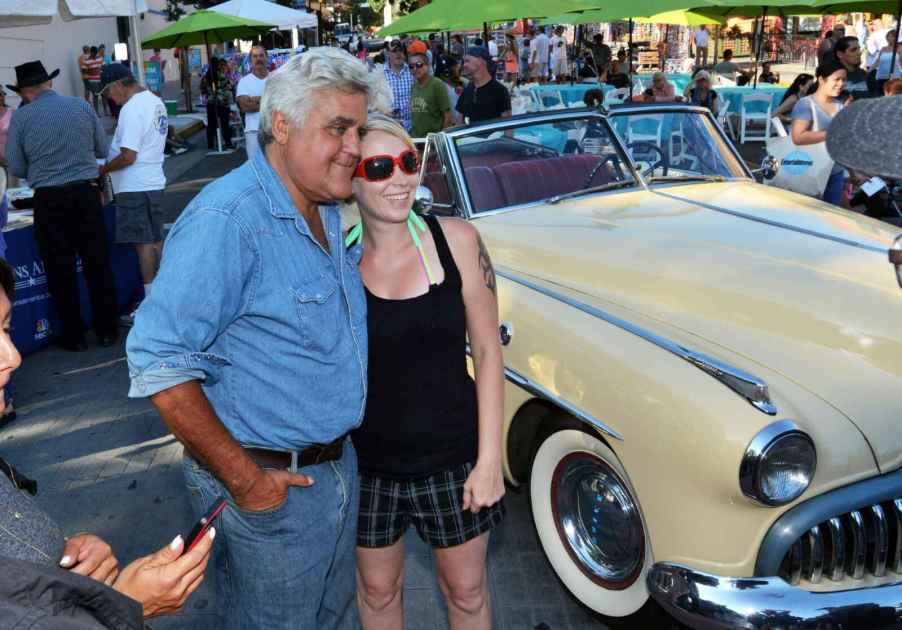 Jay Leno standing next to a fan at a classic car show in 2014