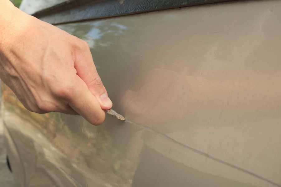A man dragging a key across a car's door, scratching it
