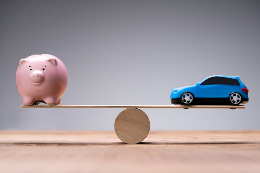 A pink piggy bank sitting on one end of a light wood seesaw with a blue toy SUV balanced on the other side depiction of 2025 tariffs
