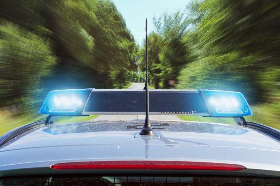 A police cruiser roof moving fast down a rural road in close rear view