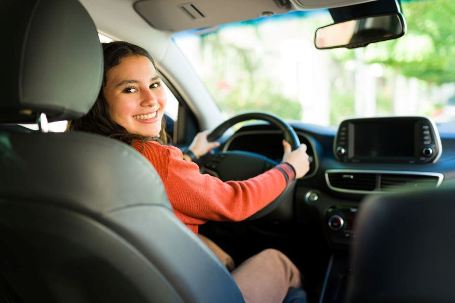 A teenage girl smiling while sitting behind the wheel of a car