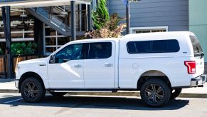 A white Ford F-150 parked on a public street with a camper shell attached