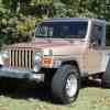 A 1999 Jeep Wrangler Sport in Desert Sand Pearl parked on grass in left front angle view