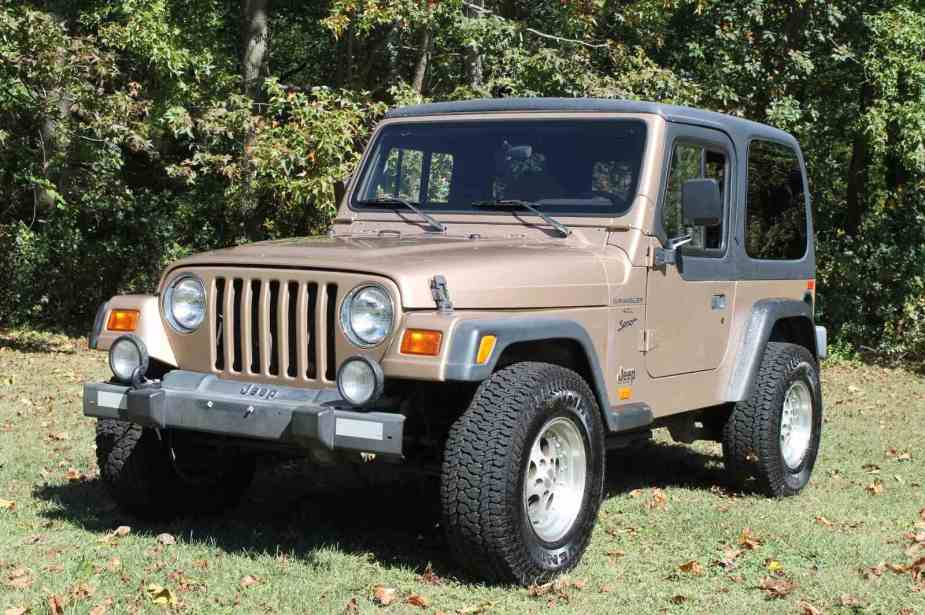 A 1999 Jeep Wrangler Sport in Desert Sand Pearl parked on grass in left front angle view