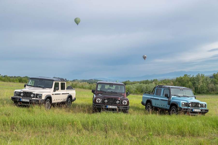 Lineup of Ineos Grenadier SUVs, which are challenging the latest Land Rover Defender, parked in a field with balloons overhead.