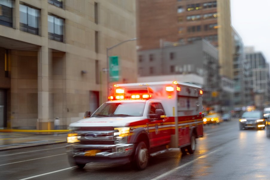 Blurry ambulance with lights and sirens driving through a city.