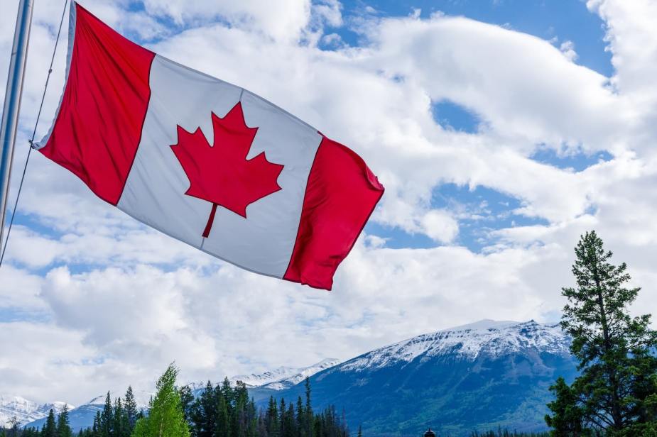 The canada flag over mountains and trees.