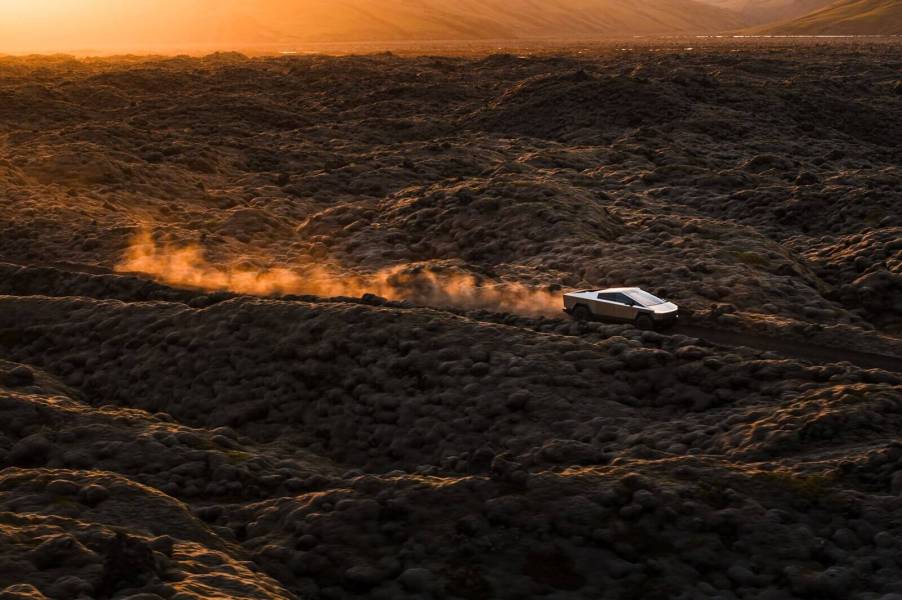 A Tesla Cybertruck, with a lower price for the new base model, drives across a trail.