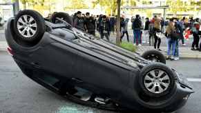 Car flipped on a city street, students looking at it.