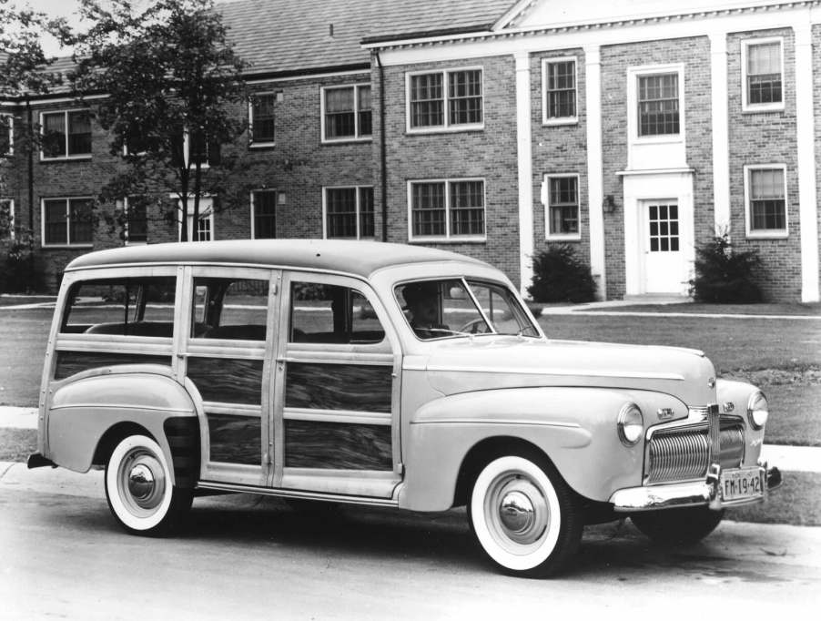 Wood-paneled Ford "woody" wagon parked in front of a brick house.