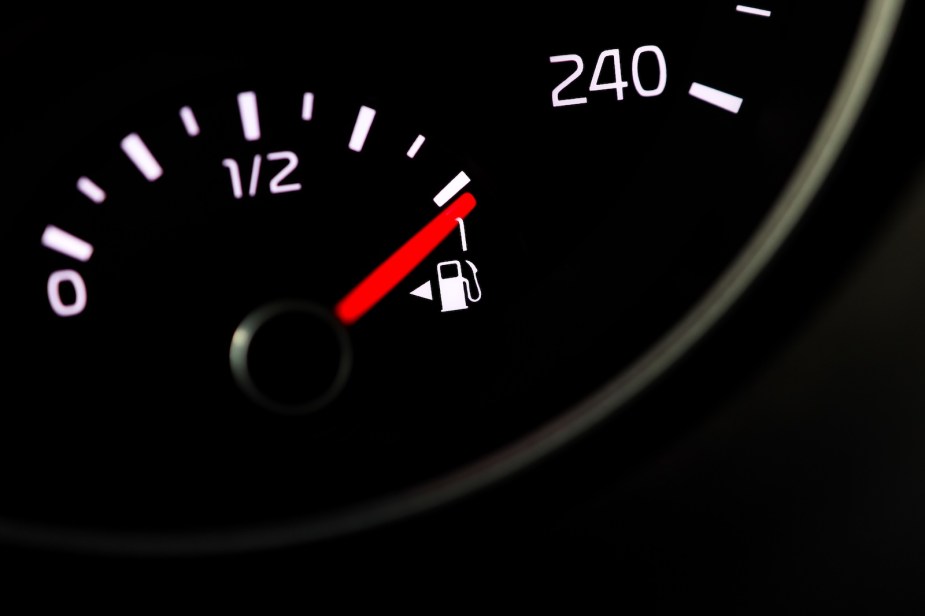 The fuel filler door arrow on a gas gauge in a black car dashboard.