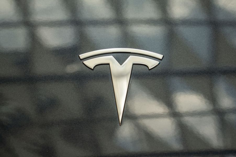 A Tesla badge on a gray EV.