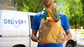 Man holding a bag of groceries in front of a delivery van.