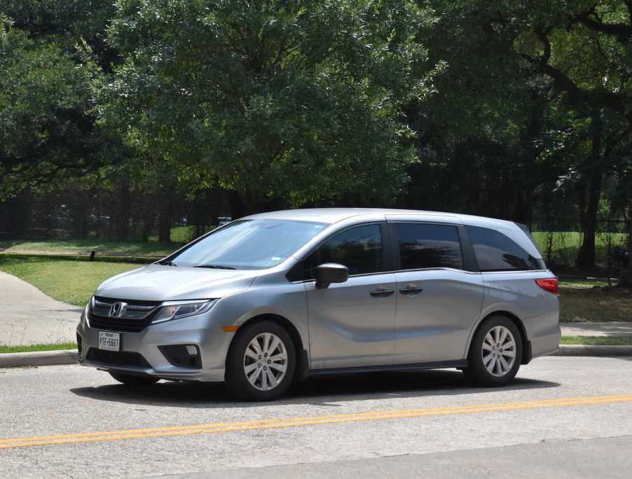 Silver Honda minivan driving down the road, trees visible in the background, after a dad bought it with a credit card.