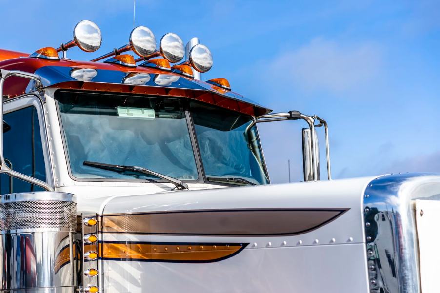 Orange and white semi truck with a roof lines in various size chrome air horn trumpets.