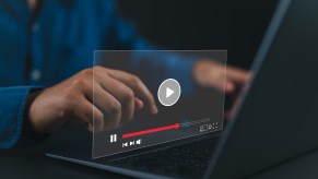 YouTube video browser hovering in front of a laptop screen, a man's hands visible in the background.