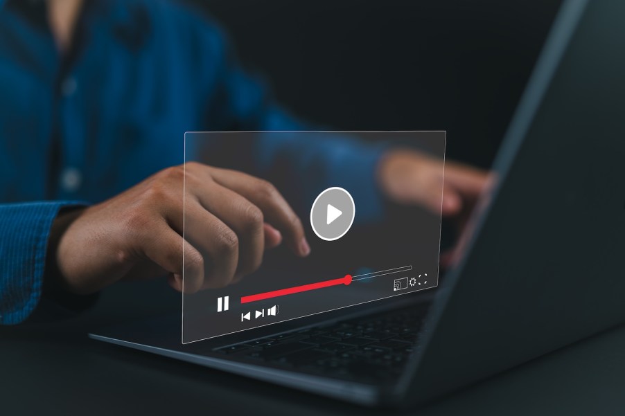 YouTube video browser hovering in front of a laptop screen, a man's hands visible in the background.