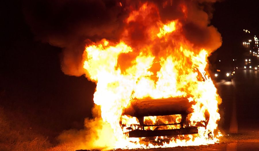 A parked car on fire in the darkness of night
