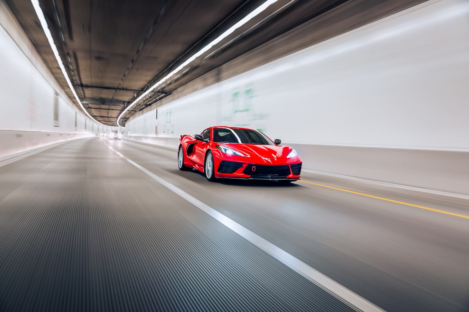 A red C8 Corvette speeding through a tunnel under overhead lights.