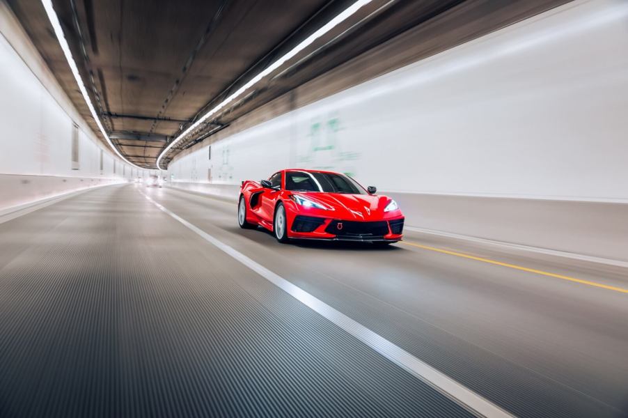 A red C8 Corvette speeding through a tunnel under overhead lights.