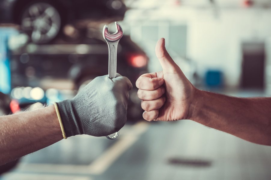 Mechanic and customer give each other thumbs-up signs in close view of hands