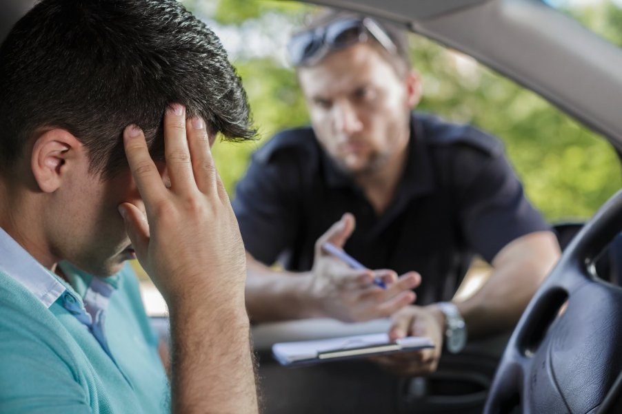 Driver with their head in their hands, a cop in the background during a police traffic stop for a suspended license because of unpaid child support