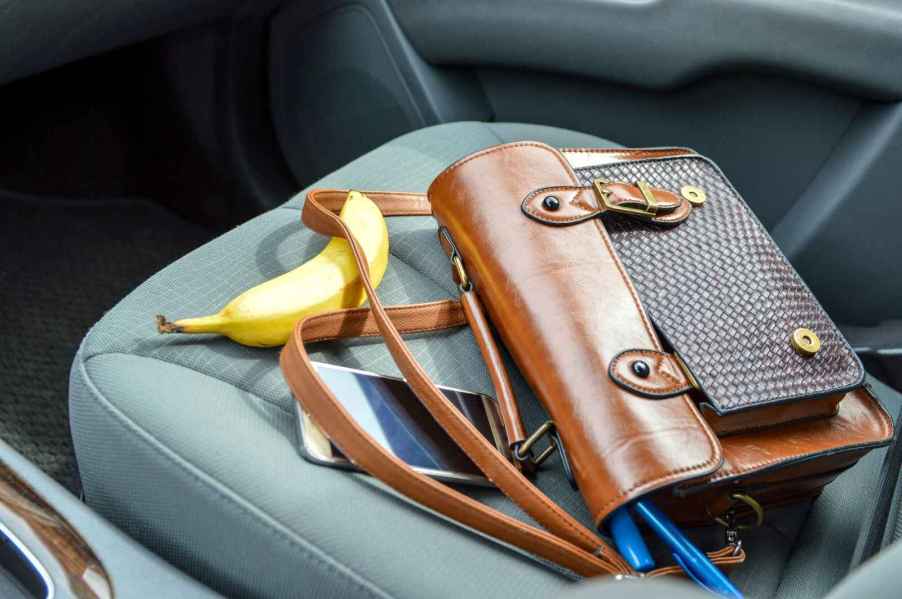 A purse sitting on a car's passenger seat with a banana and a cell phone