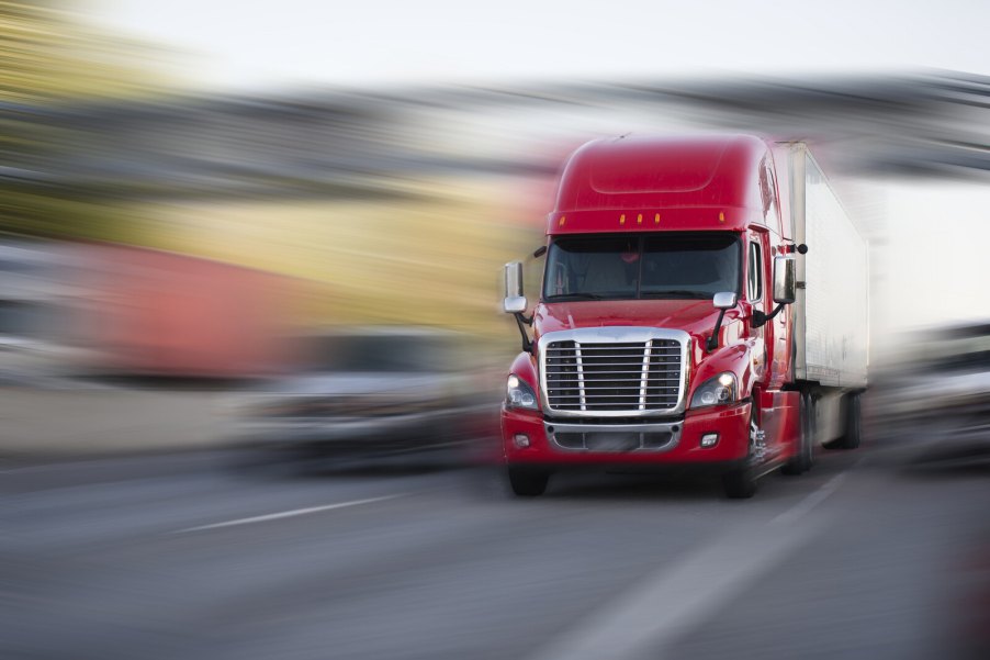 A red semi-truck driving fast on freeway blurred background