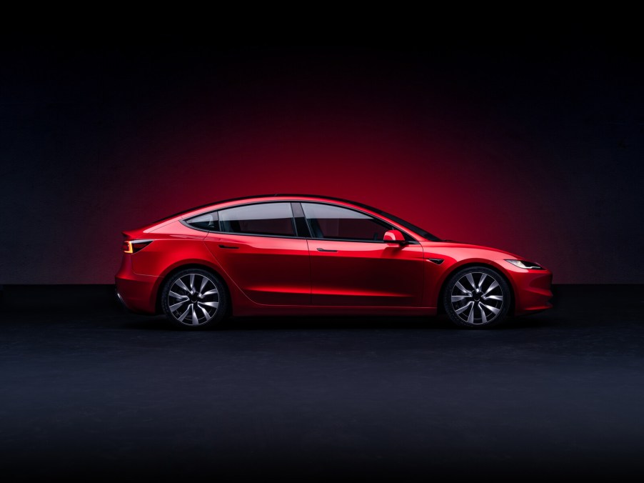 A red Tesla Model 3 rendering in full right profile view on dark, shadowy background