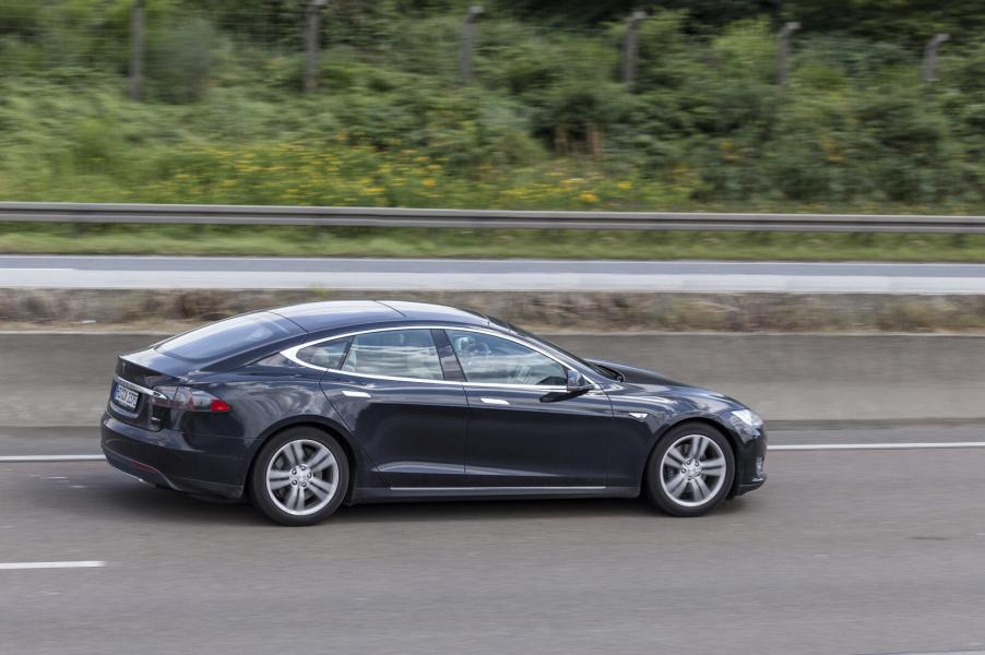 A black Tesla Model S driving on a highway in full right profile view