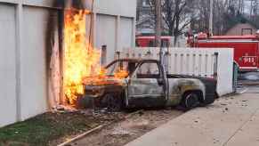 A truck on fire, sitting against a building