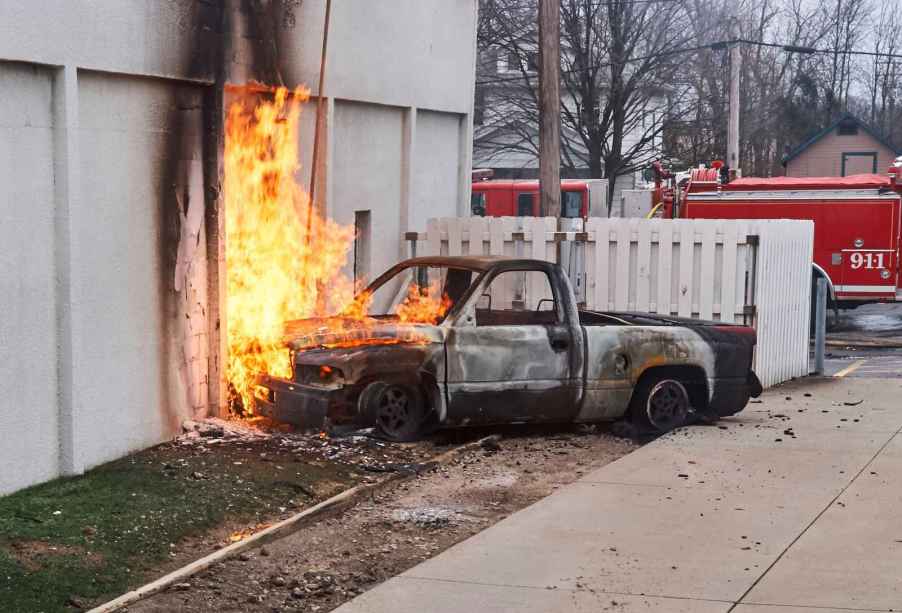A truck on fire, sitting against a building