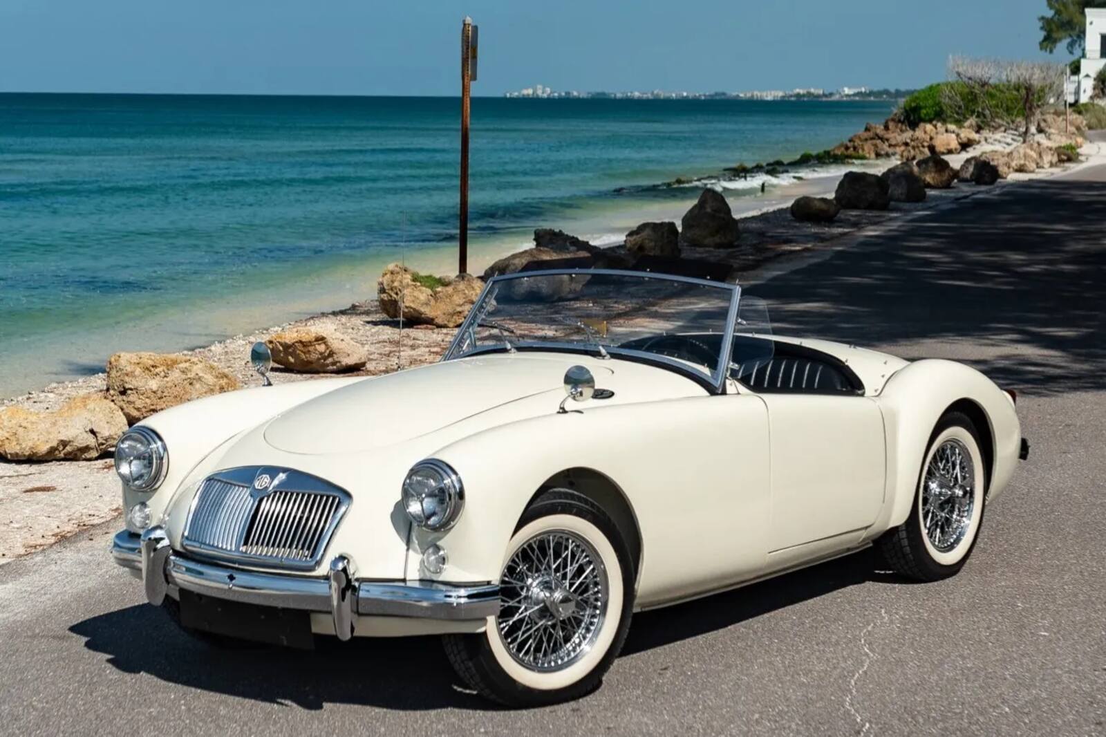 A white 1959 MGA 1500 roadster parked on a beach in left front angle view