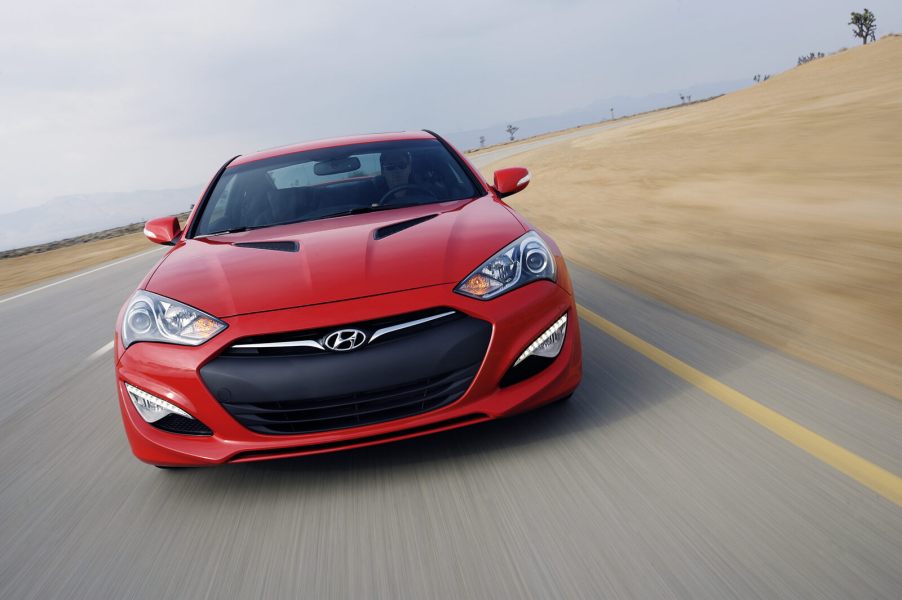 A red 2013 Hyundai Genesis Coupe driving on a paved road in direct front view
