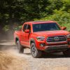 An orange 2016 Toyota Tacoma driving on a dusty gravel road