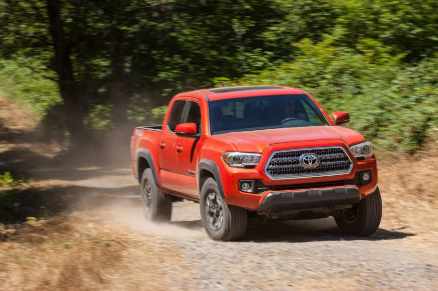 An orange 2016 Toyota Tacoma driving on a dusty gravel road