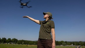 Woman in a green police uniform launching a quad copter drone.