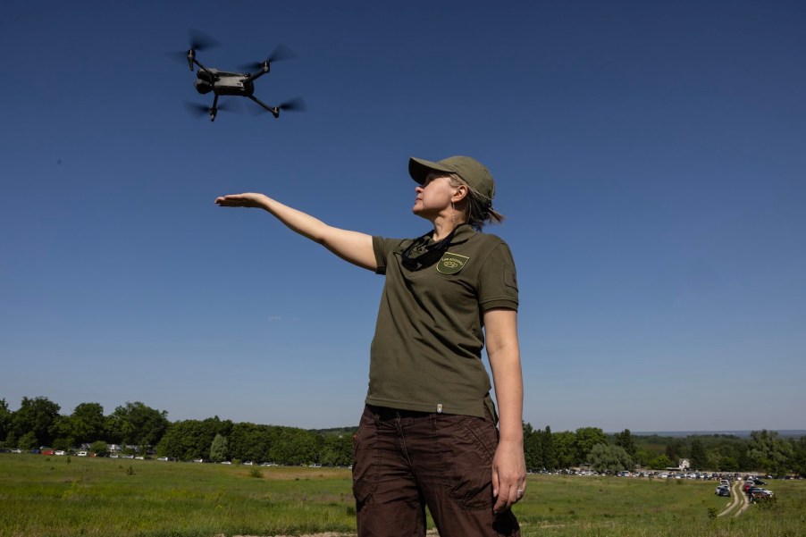 Woman in a green police uniform launching a quad copter drone.
