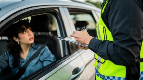 Police officer writing a driver a ticket because she forgot her license, a shock on her face.