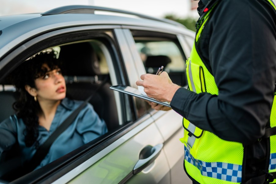 Police officer writing a driver a ticket because she forgot her license, a shock on her face.