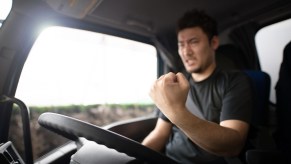 Semi truck drive angry at motorist who passes them and slows down, shaking his fist.