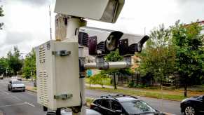 Speed cameras film cars passing by on a city street, trees visible in the background.