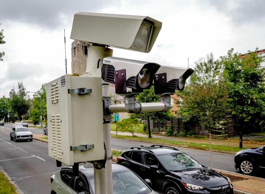 Speed cameras film cars passing by on a city street, trees visible in the background.