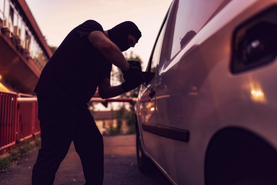 Thief pries open stolen Kia car, the sunset visible in the background.