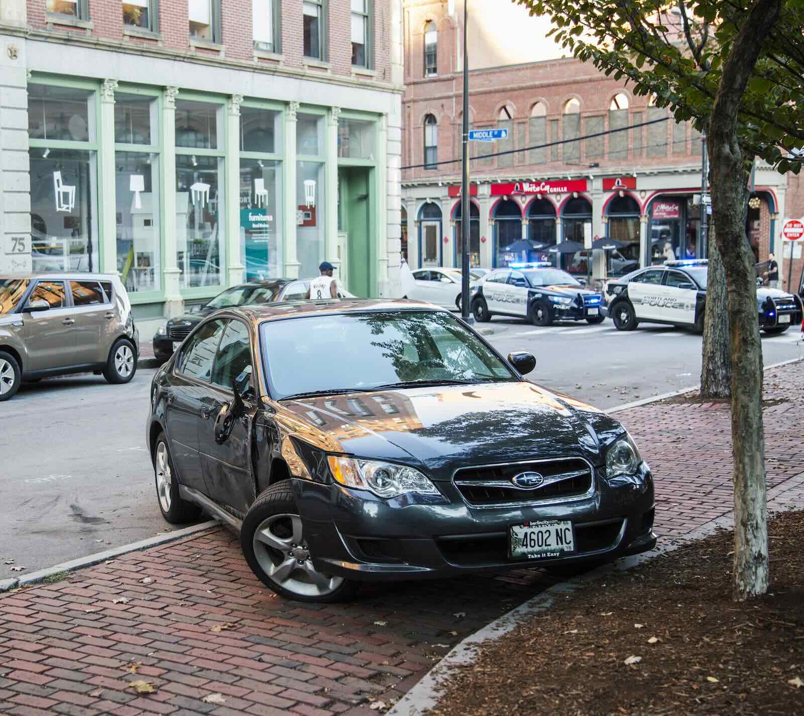 Subaru WRX sedan totaled by dealership manager, police cars visible in the background.