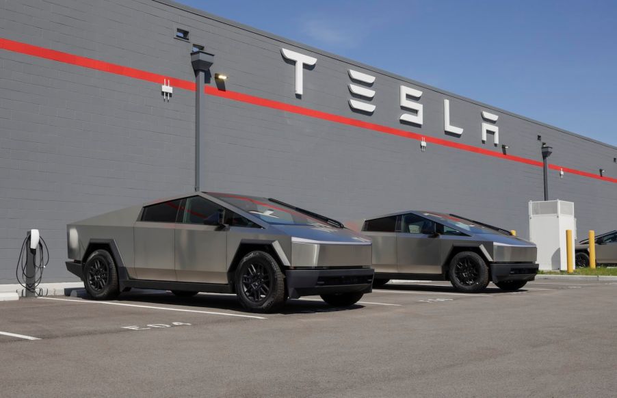 Two Cybertrucks parked underneath the Tesla sign at a dealership showroom service center